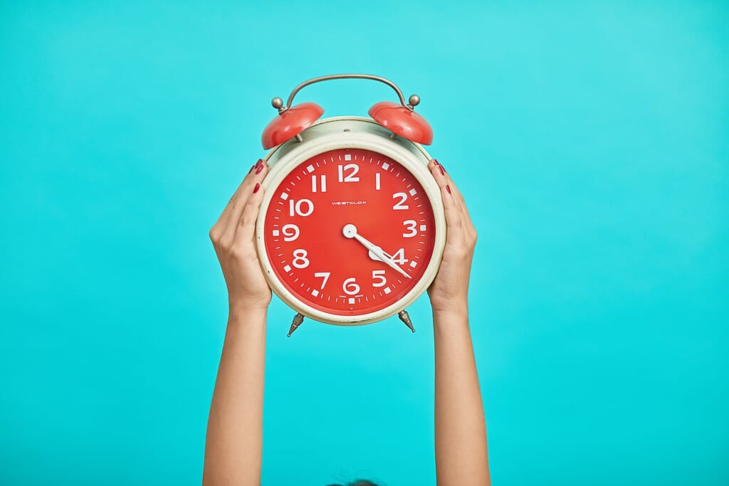 person holding red and beige twin bell analog alarm clock