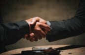 two people shaking hands over a wooden table