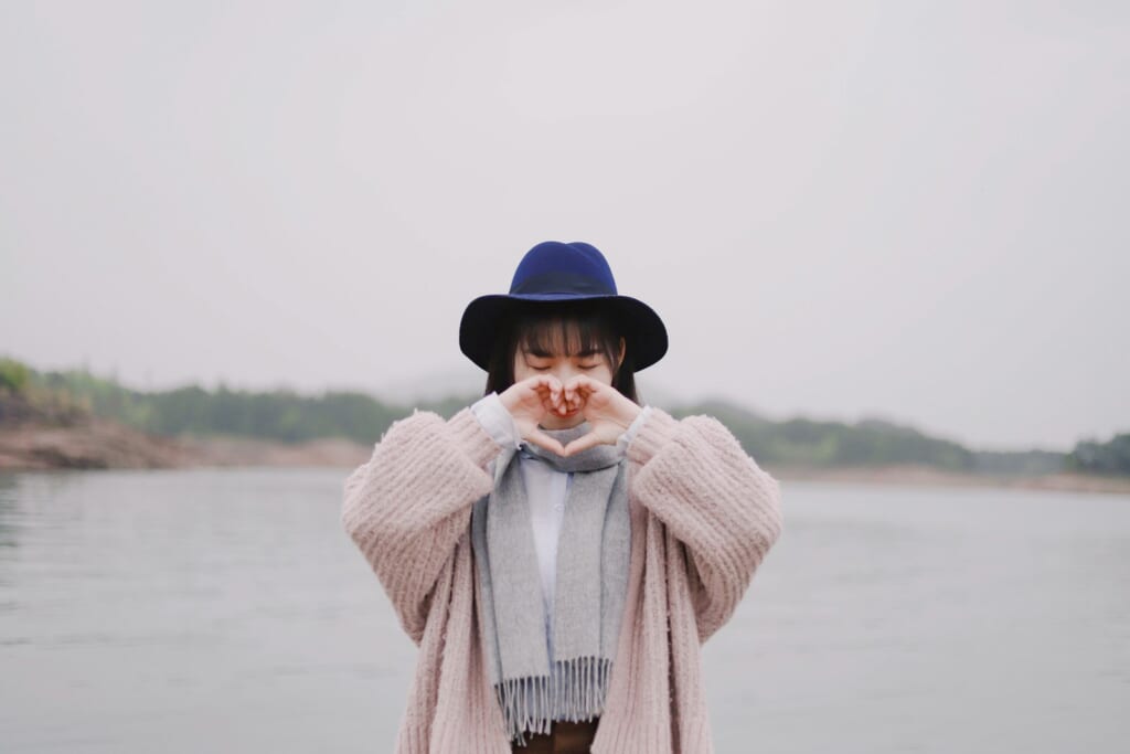 woman forming heart by hand near water