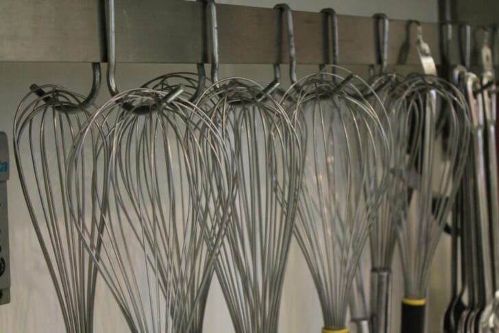 a bunch of whisks hanging on a wall