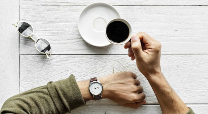 男性がコーヒーを飲みながら腕時計を見ている写真