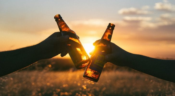 夕日をせにビールグラスで乾杯する写真